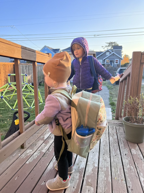 Ingrid standing with her backpack, ready to go to school. The backpack is as big as she is!
